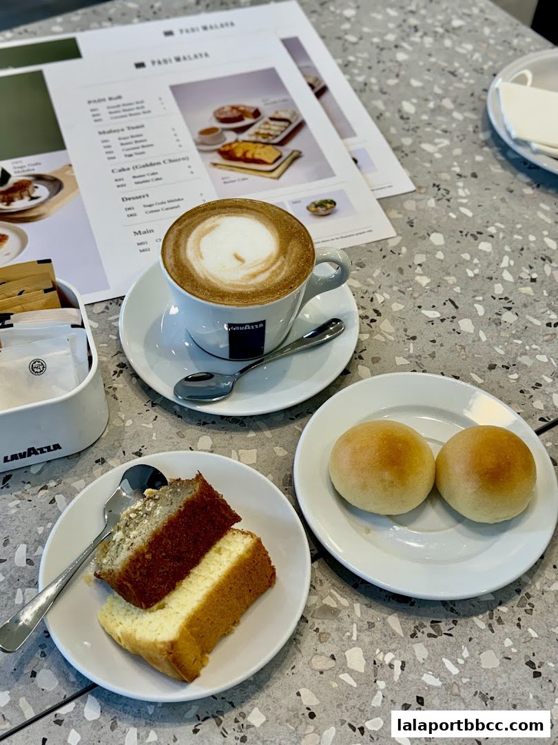 A table setting with coffee, cake slices, and bread rolls, with a menu in the background.