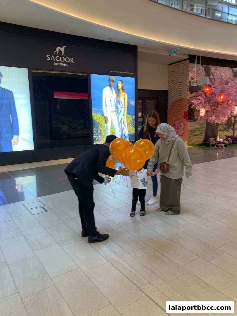 A store employee hands balloons to a child in front of a fashion store.
