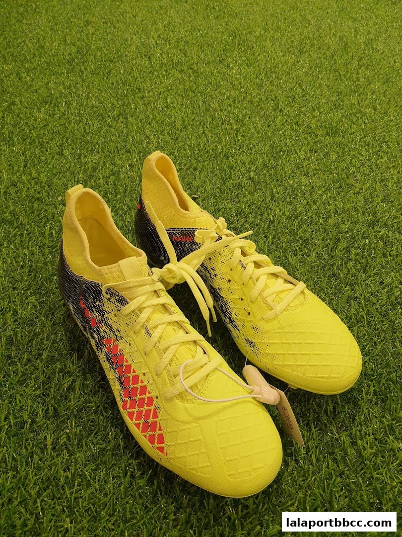 A pair of bright yellow soccer cleats with red accents on a green grassy surface.