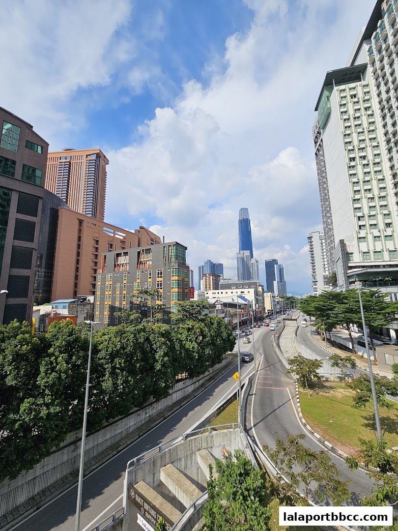 A cityscape view of Kuala Lumpur with tall buildings and a highway under a cloudy sky.