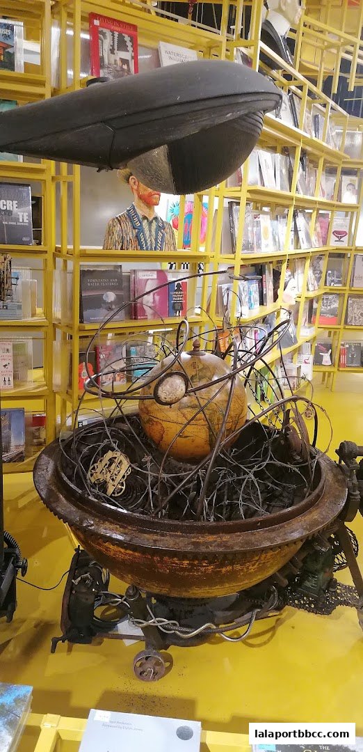 A unique art installation featuring a globe within a rusty metal structure, surrounded by bookshelves.