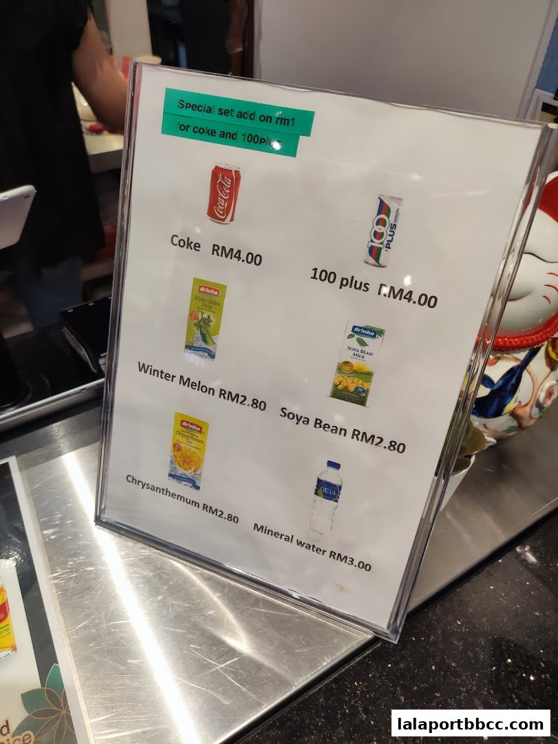 A menu board displays various drinks and their prices at Nam Heong Chicken Rice.