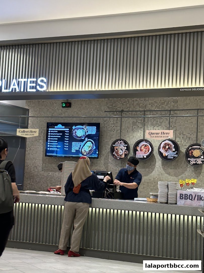 Customers ordering food at a counter with a digital menu and staff serving.