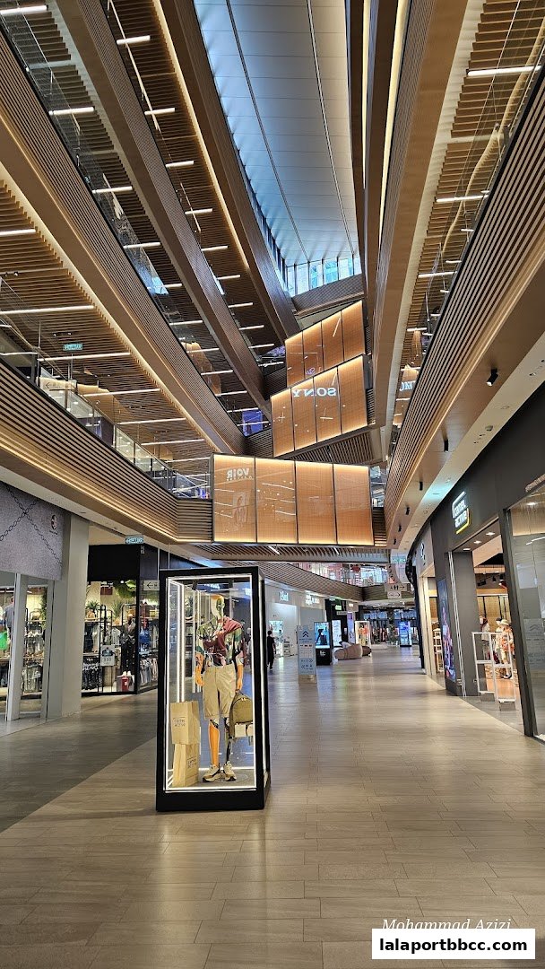 A modern shopping mall interior with multiple levels and shops, featuring a mannequin display.