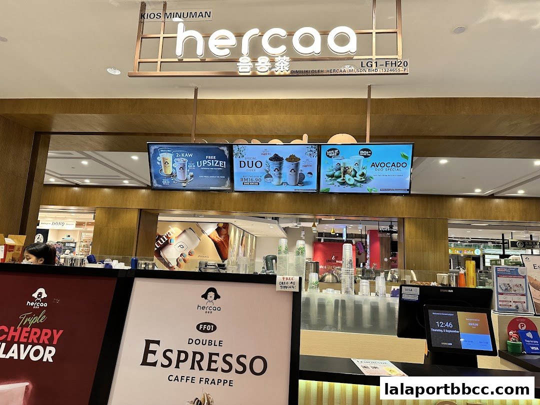 The front counter of a beverage shop called Hercaa, displaying menu screens and promotional items.