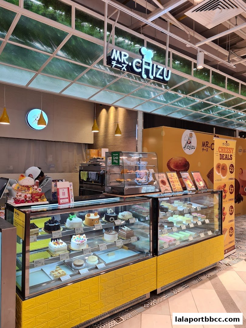 A brightly lit dessert shop with a display case full of colorful cakes and pastries.