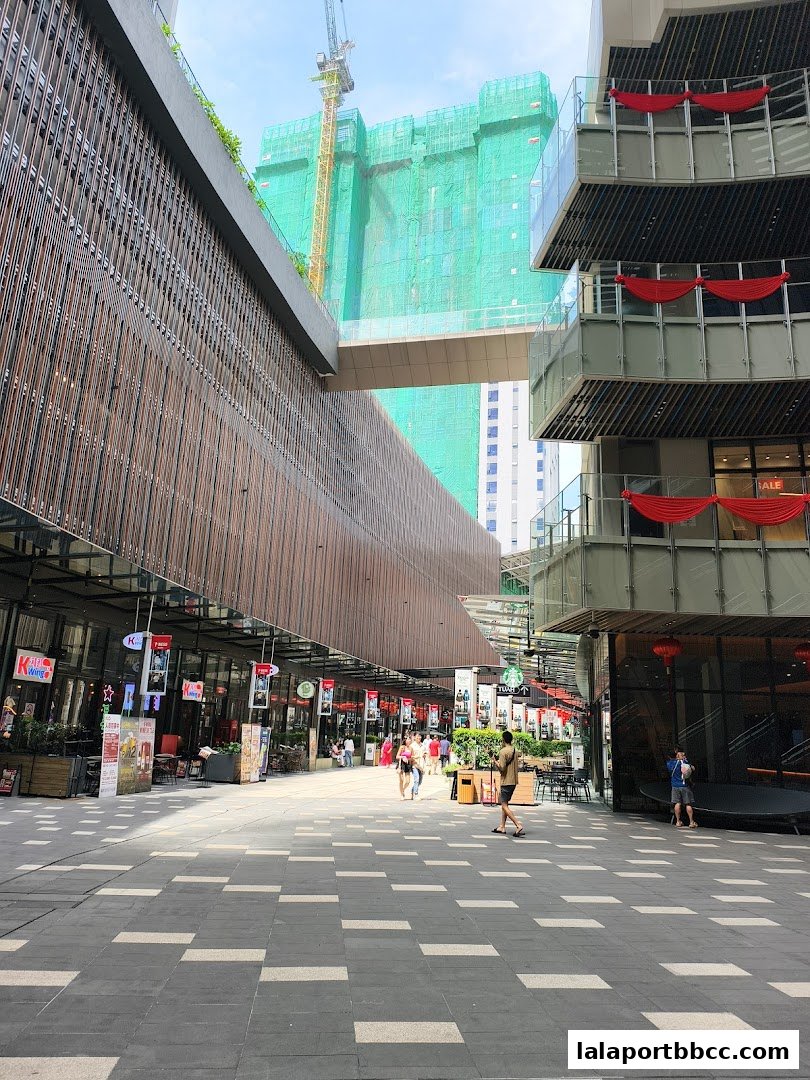 A pedestrian walkway in a modern shopping area with shops and a building under construction.