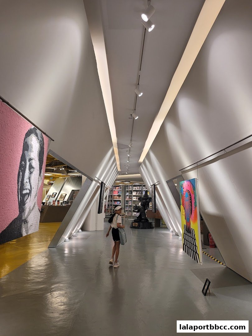 A young girl walks down a modern hallway with art installations and a bookstore in the background.
