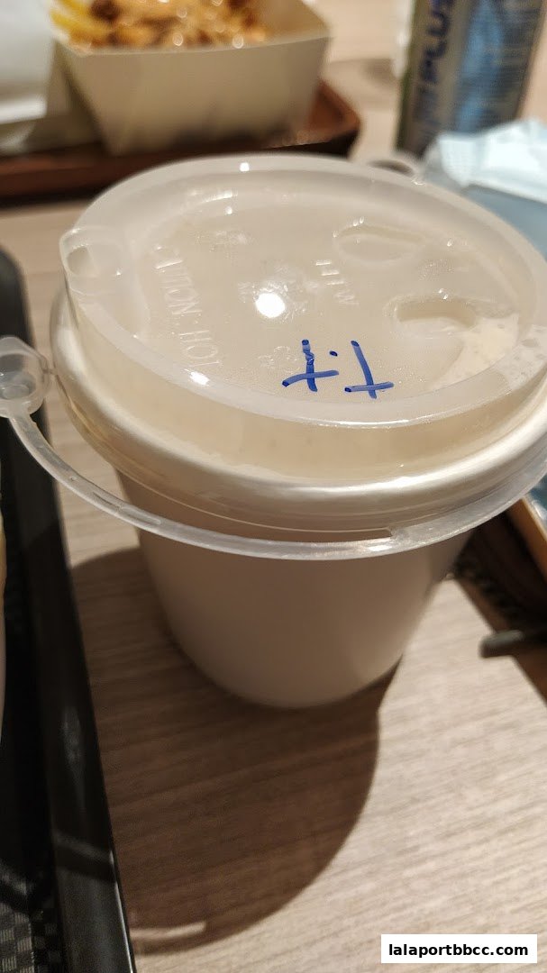 A close-up of a white cup with a clear lid, marked with blue ink.