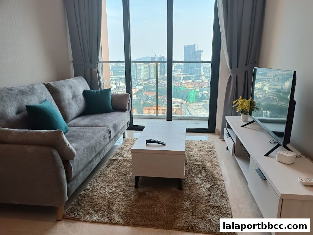 A modern living room with a sofa, coffee table, and TV, offering a city view.