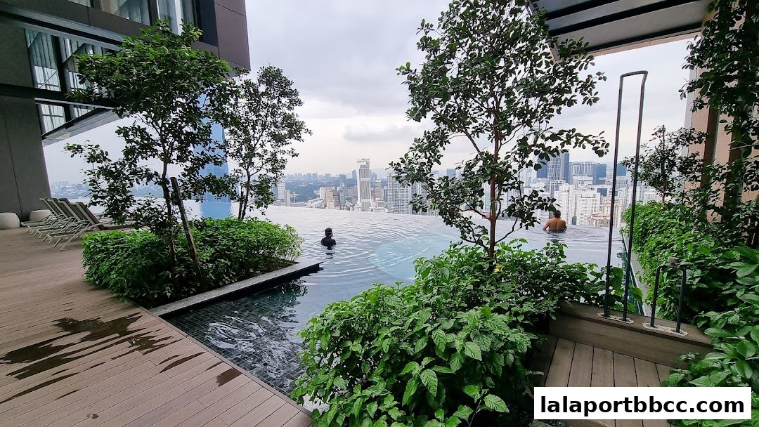 Infinity pool with lush greenery and city skyline view, featuring people relaxing.