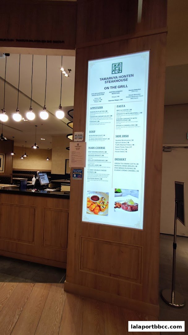 A digital menu board for Tamaruya Honten Steakhouse, showcasing various dishes and prices.