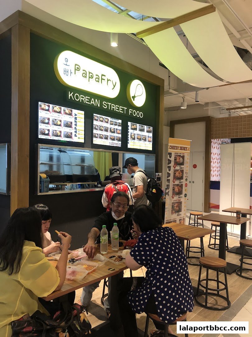 People dining at tables in front of a Korean street food stall called PapaFry.