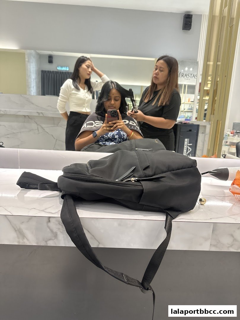 A customer is getting her hair styled by a stylist, with another stylist standing nearby.