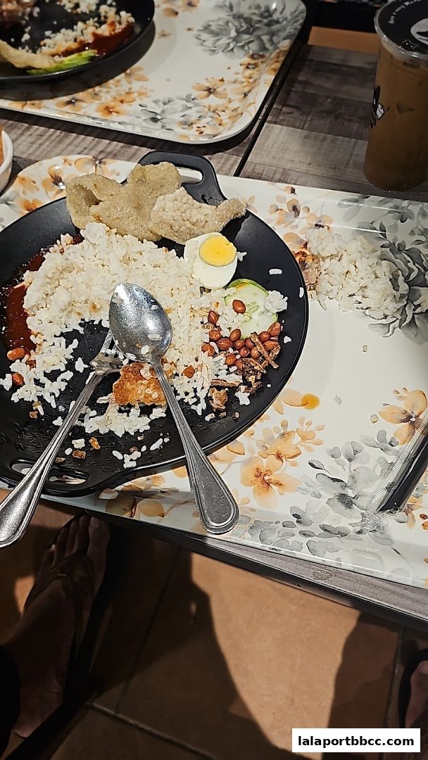 A plate of nasi lemak with a hard-boiled egg, cucumber, peanuts, and crackers, partially eaten.