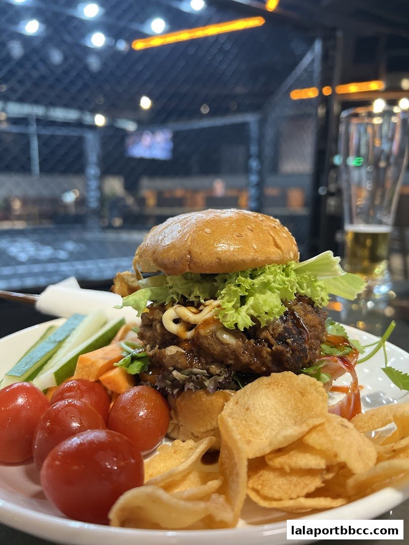 A gourmet burger served with cherry tomatoes, cucumber sticks, and chips on a white plate.