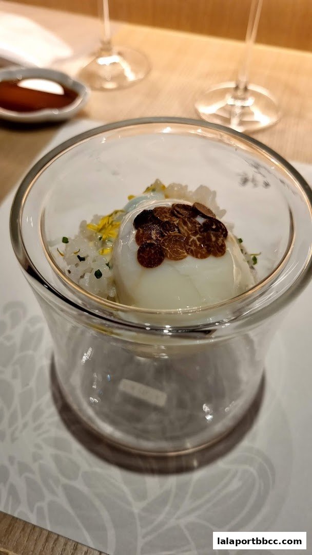 A close-up of a gourmet dish with rice, a poached egg, and truffle shavings in a glass bowl.