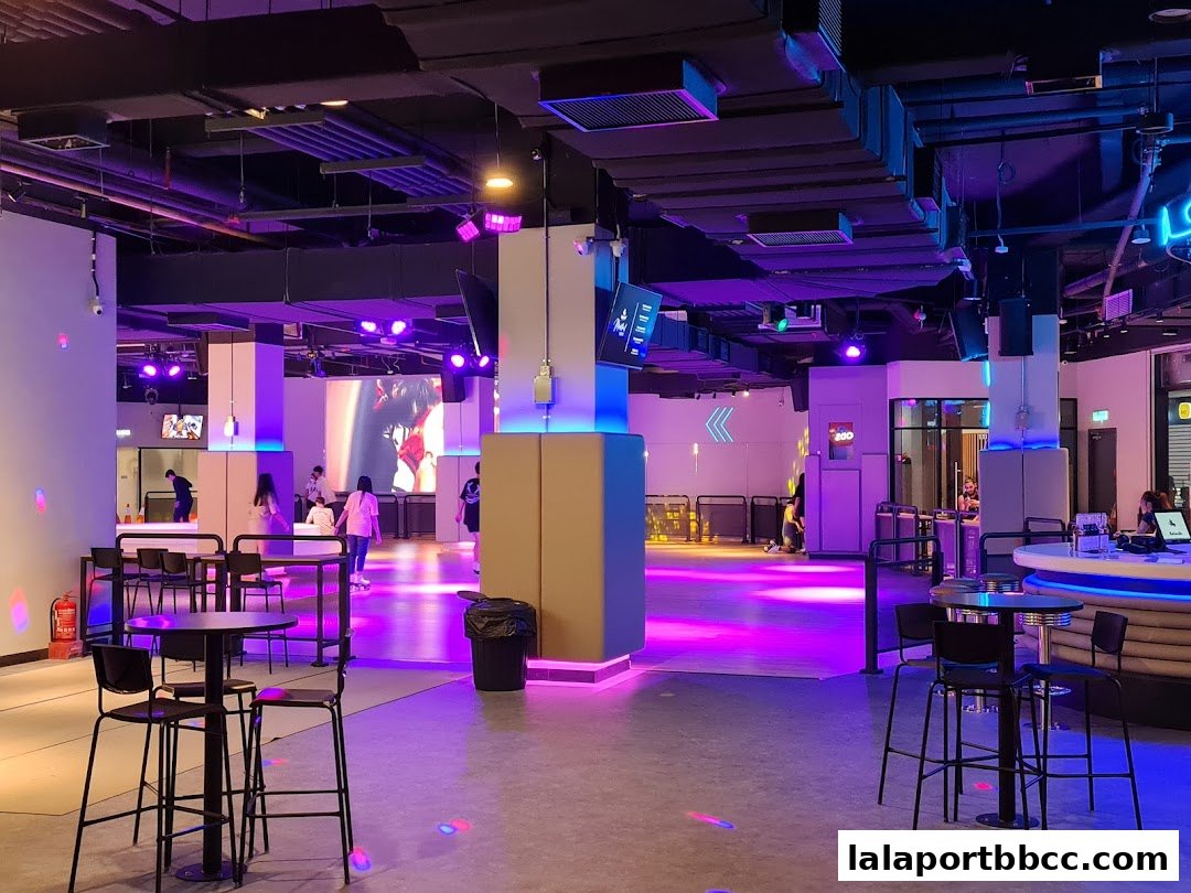 Interior of a roller skating rink with neon lights, seating areas, and people skating.