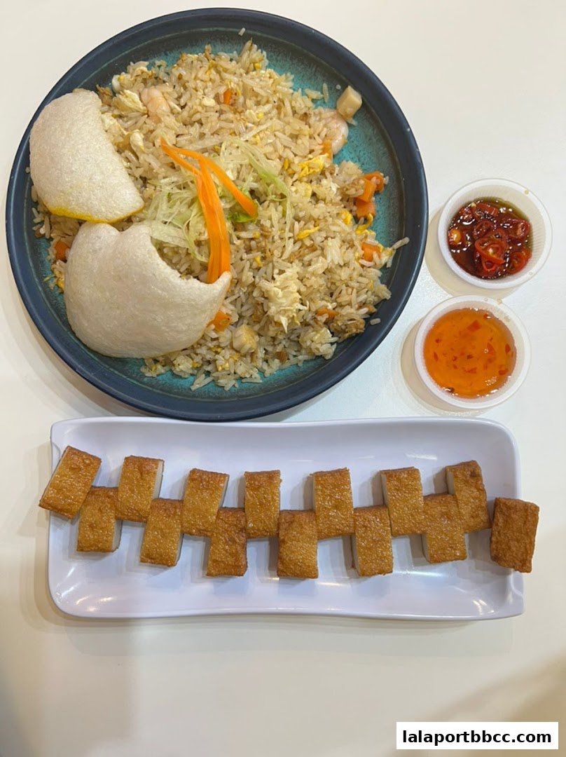 A plate of fried rice with shrimp and crackers, served with fried fish cakes and dipping sauces.