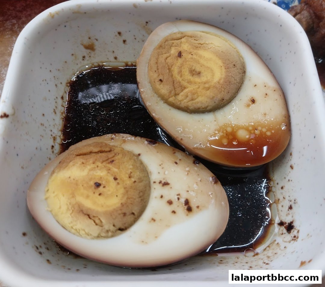 Two halves of braised eggs in a white bowl with dark sauce.