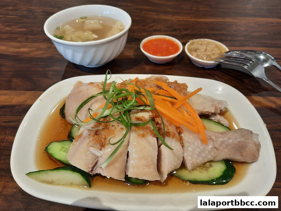 A plate of delicious chicken rice with soup and chili sauce, garnished with cucumber and carrots.