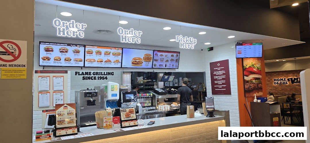 Burger King counter with digital menus displaying burgers and chicken, and staff preparing orders.