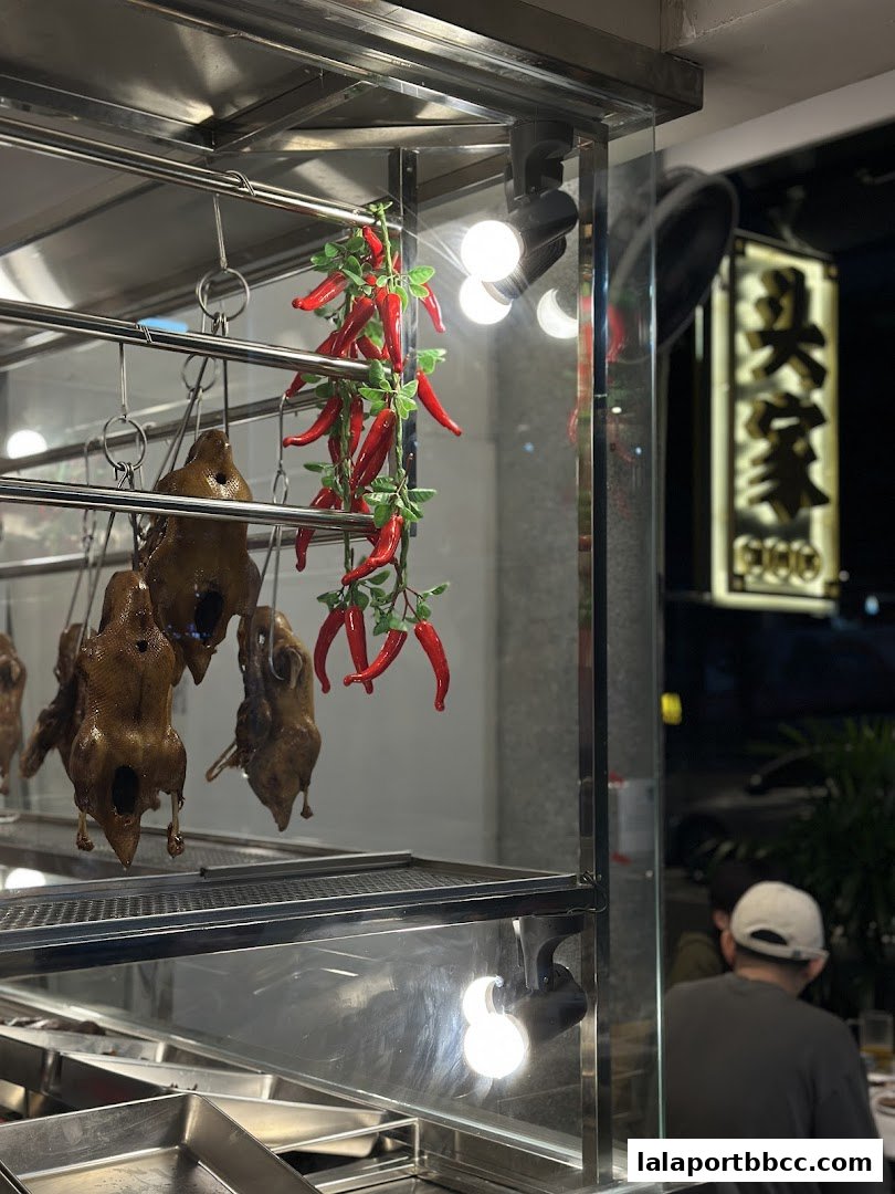 Roasted ducks hang in a display case with decorative red chilies and bright lights.
