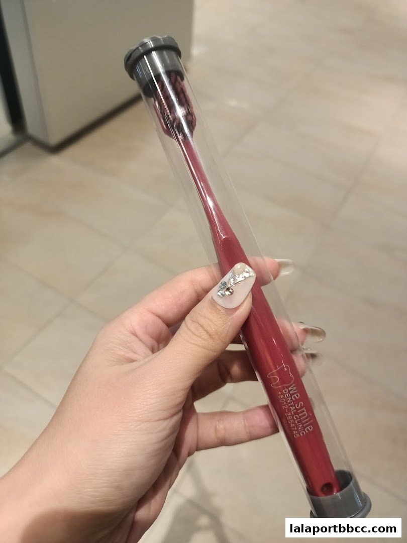 A hand holds a red toothbrush in a clear protective case with the WeSmile Dental Clinic logo.