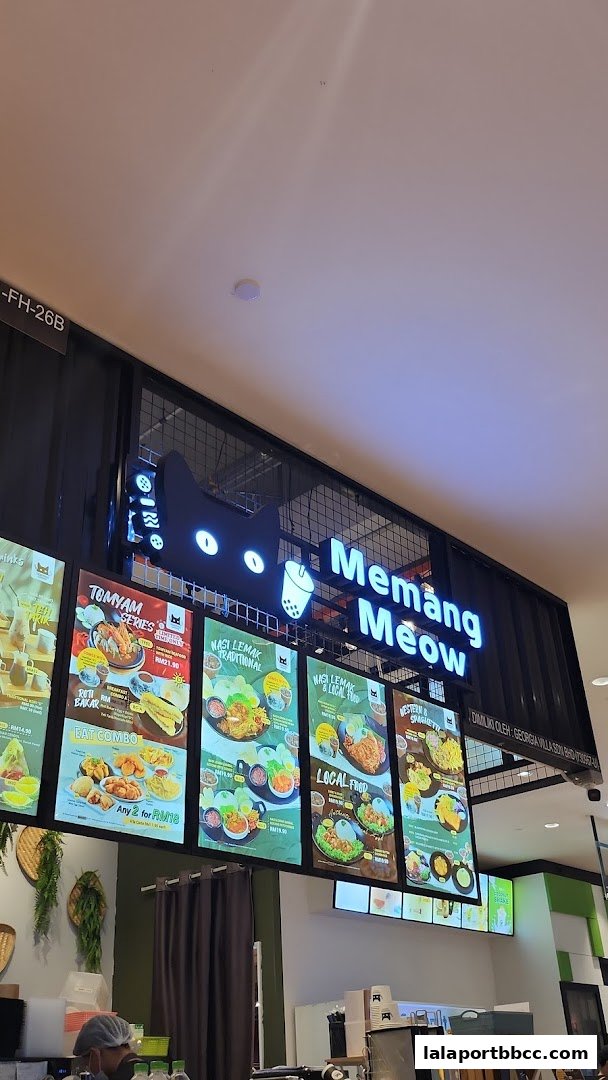 A brightly lit food stall with a prominent cat logo and illuminated menu boards displaying various dishes.
