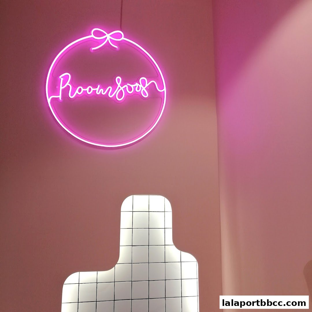 A pink neon sign with the text 'Room 8008' hangs on a pink wall above a tiled light fixture.