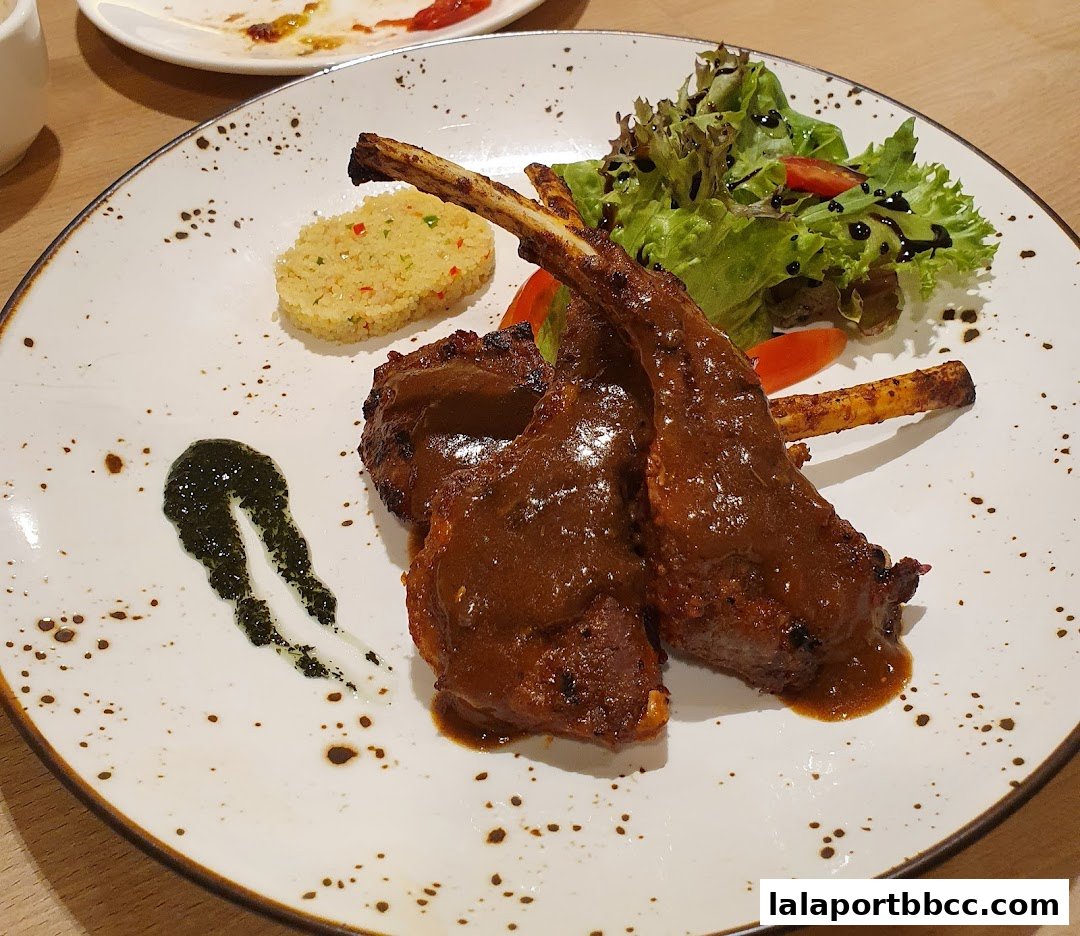 A plate of lamb chops with a side salad and couscous, drizzled with sauce.