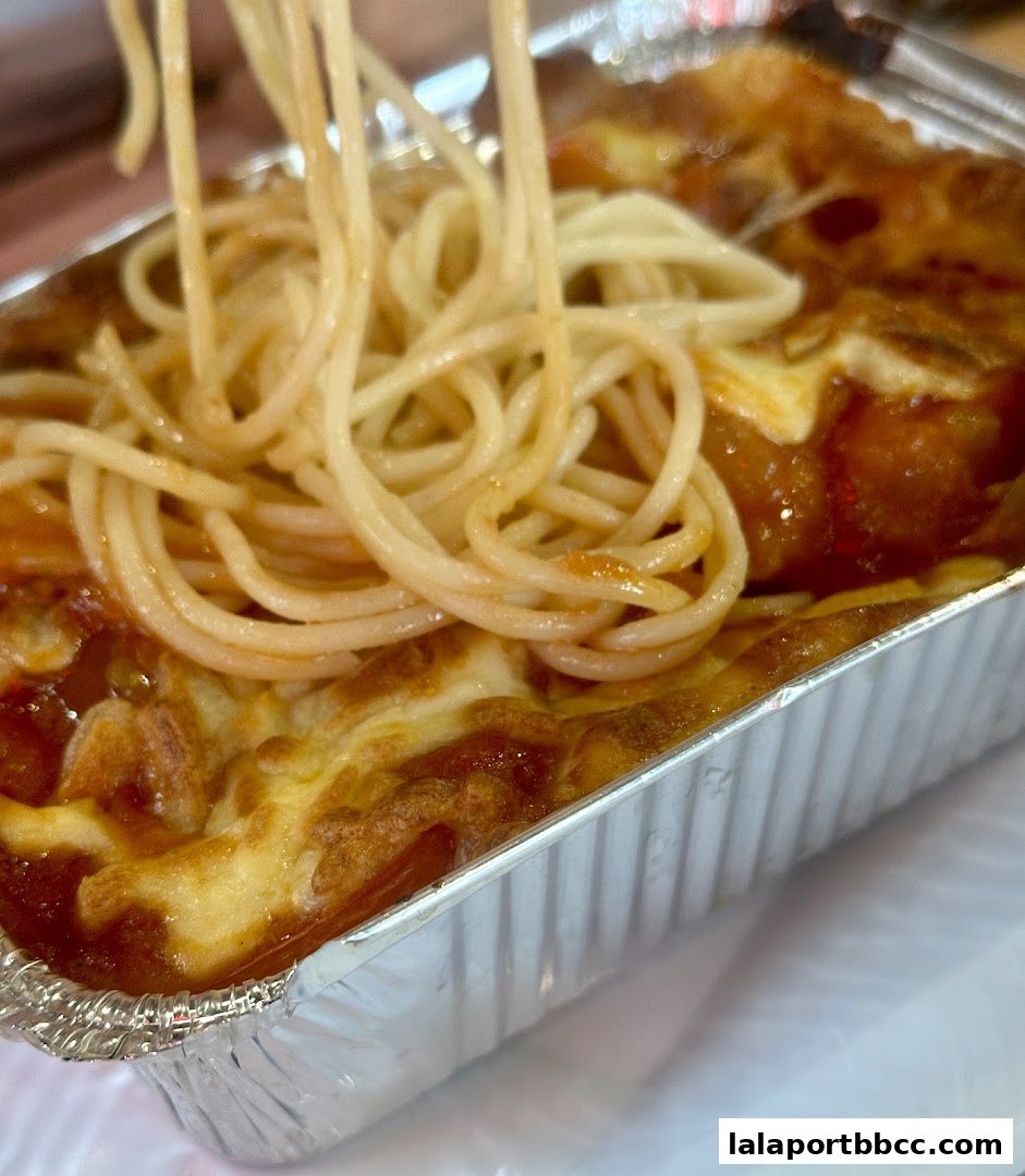 A close-up shot of spaghetti with melted cheese and tomato sauce in a foil container.
