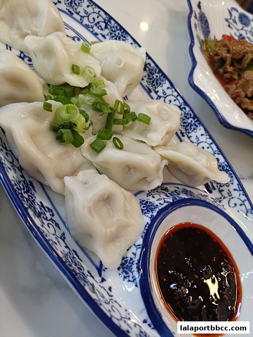 A plate of delicious dumplings with a side of dipping sauce and a dish of stir-fried beef.