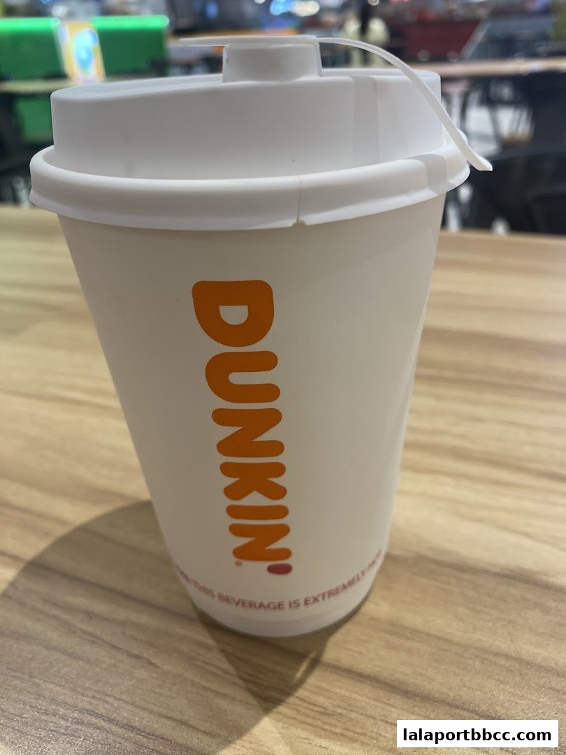 A close-up of a Dunkin' Donuts branded cup with a white lid and a white plastic tab.