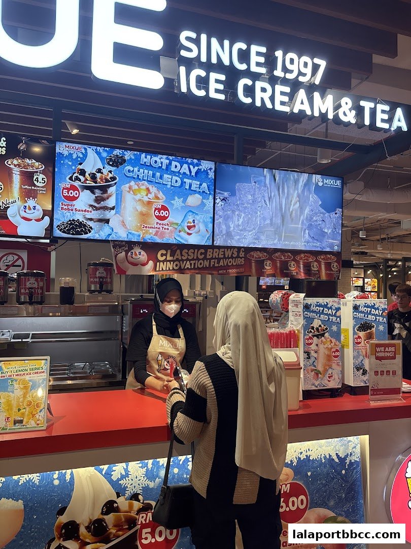 A customer orders ice cream and tea at a MIXUE counter with digital menu displays.