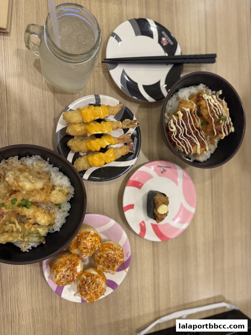 A variety of sushi dishes and a drink are arranged on a wooden table.