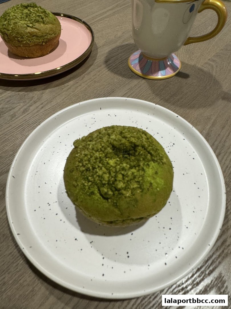 Two green matcha muffins are presented on plates with a decorative mug in the background.