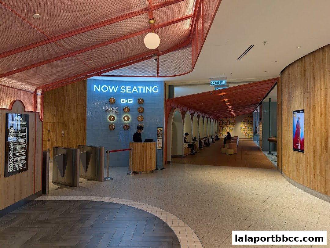 Interior view of a cinema lobby with seating areas and a 'Now Seating' display.