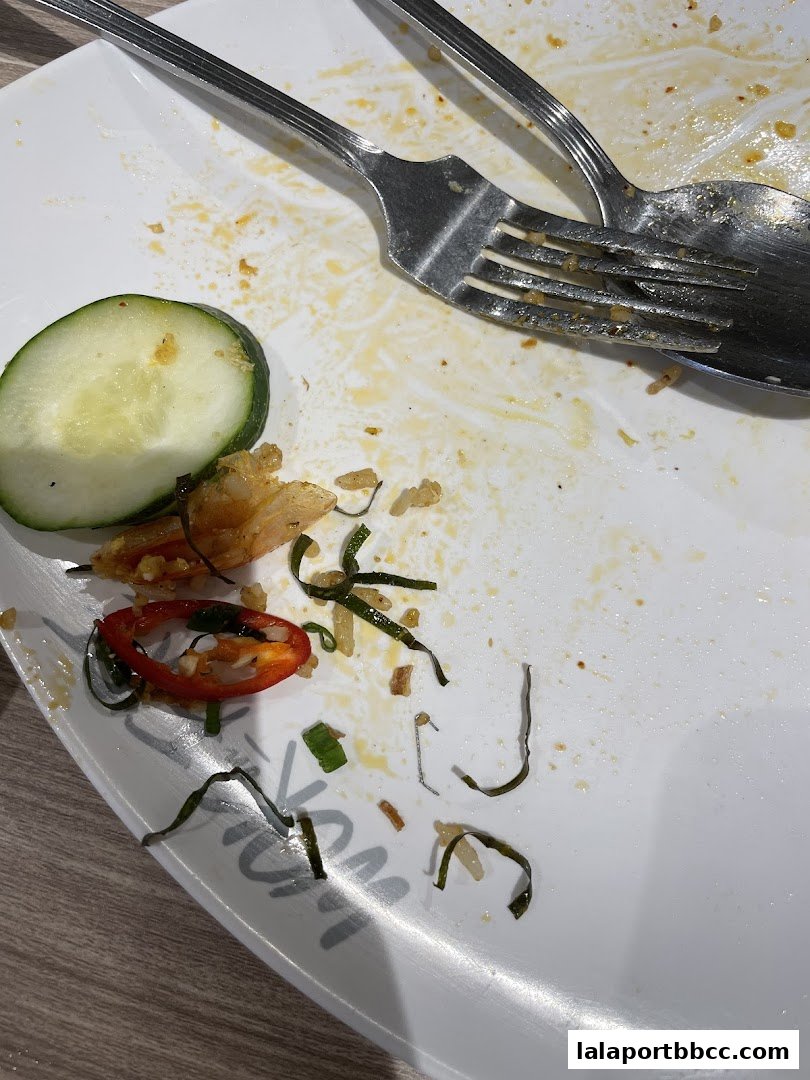 A dirty plate with leftover food, cutlery, cucumber, chili, and herbs.