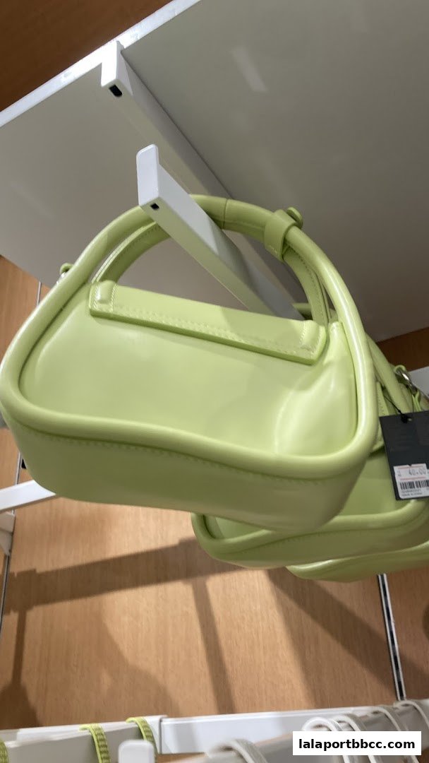 A close-up shot of a lime green handbag with a tag attached, displayed on a shelf.
