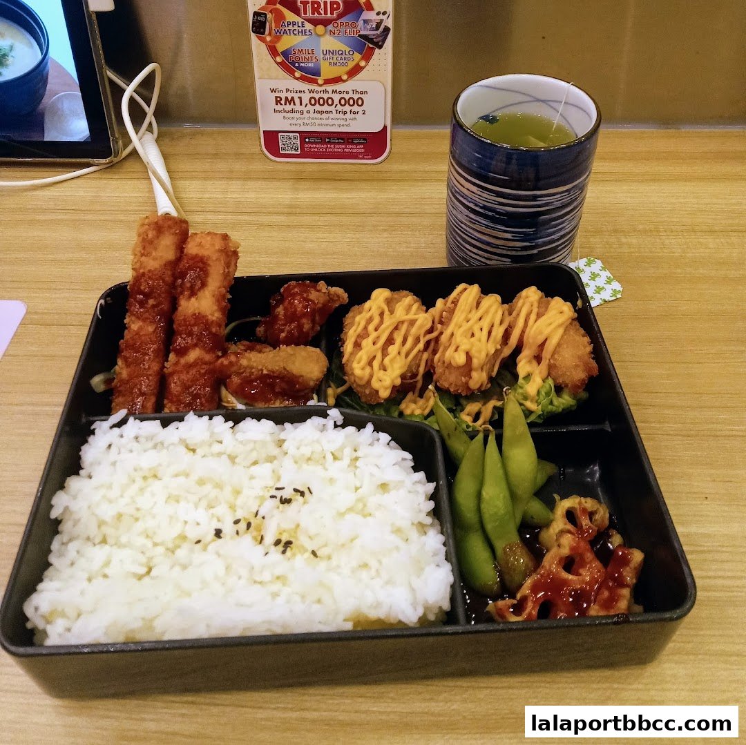 A bento box with rice, fried items, edamame, and a cup of green tea.