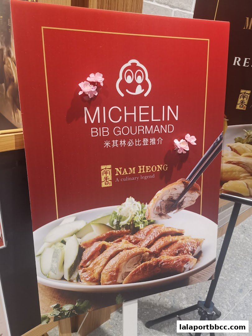 A sign for Nam Heong Chicken Rice featuring a Michelin Bib Gourmand award and a plate of roasted chicken.