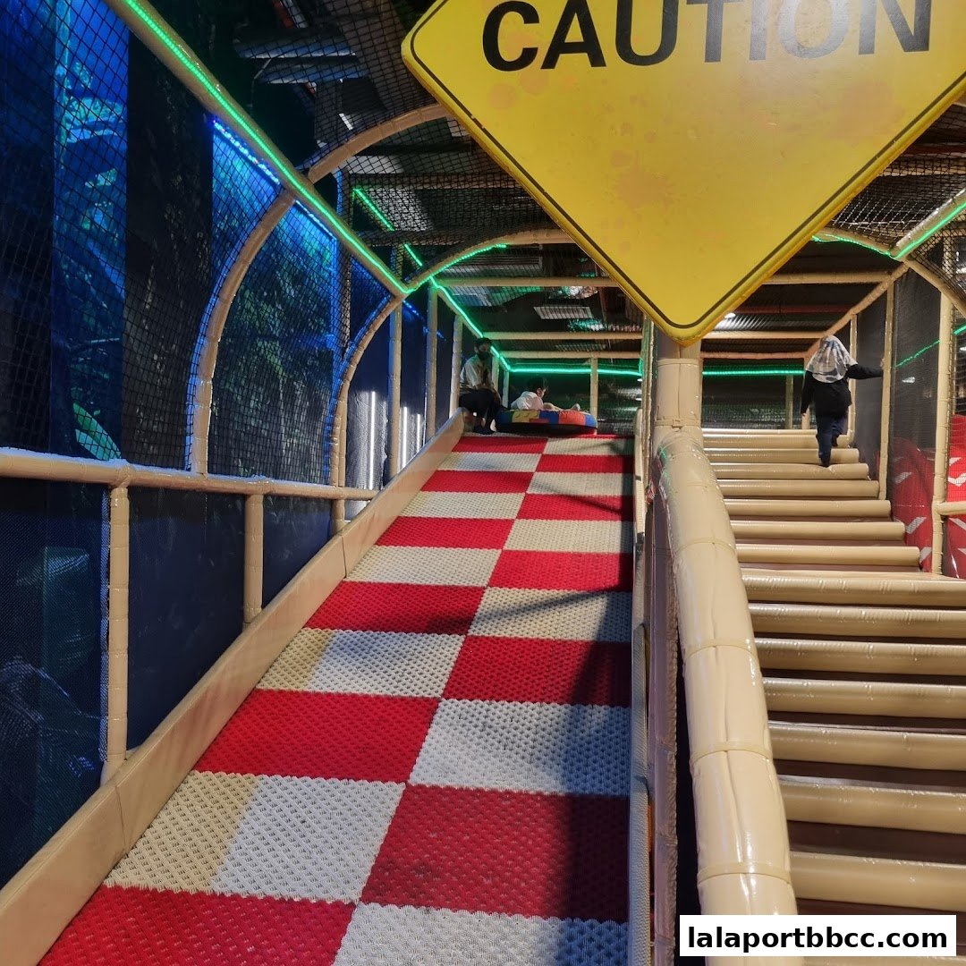 An indoor playground with a checkered slide and stairs, featuring colorful lights and a caution sign.