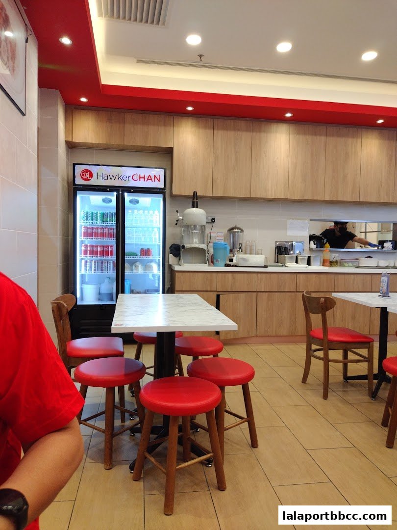 Interior of Hawker Chan restaurant with seating, a refrigerator, and kitchen counter.