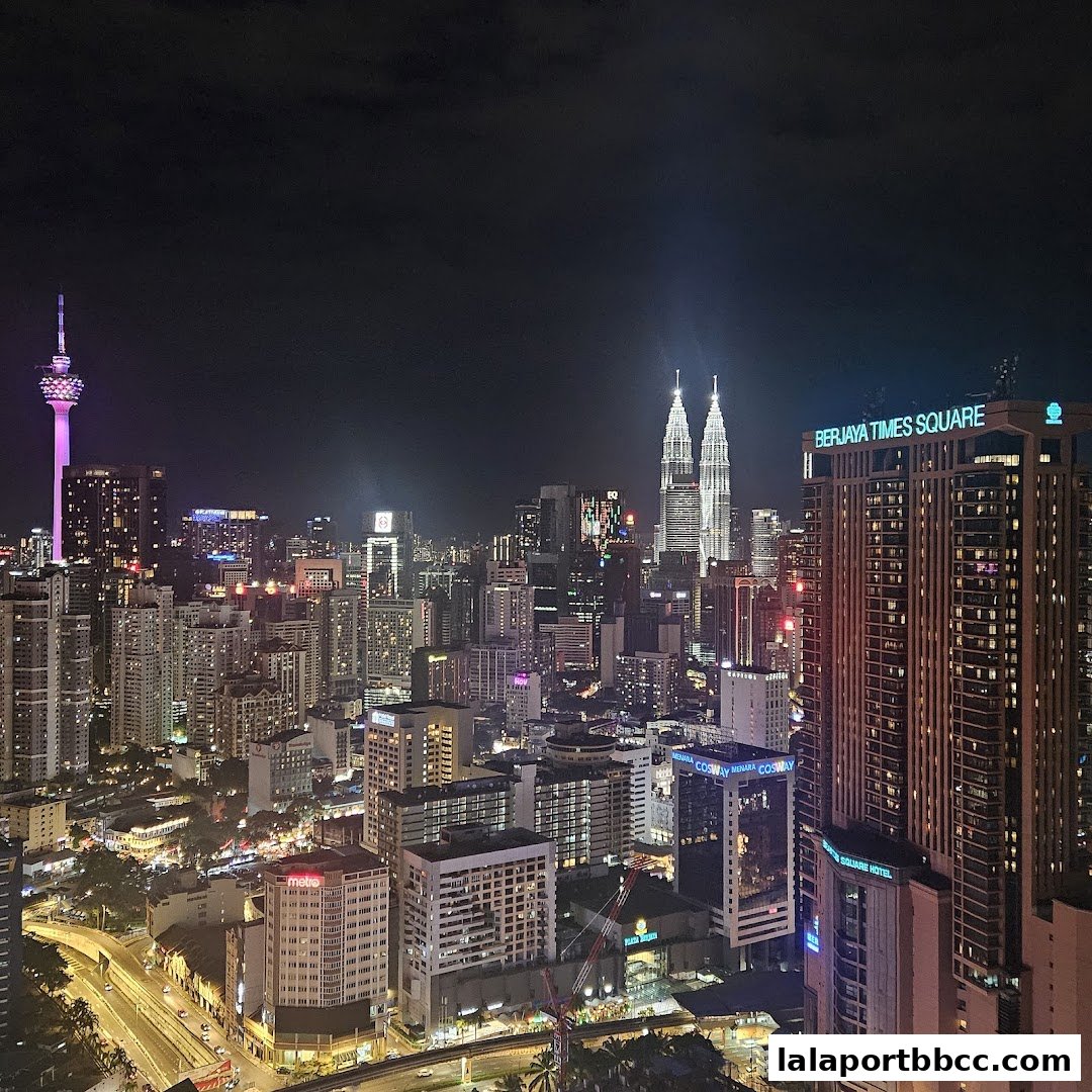 A nighttime aerial view of a bustling cityscape with illuminated skyscrapers and the Petronas Towers.