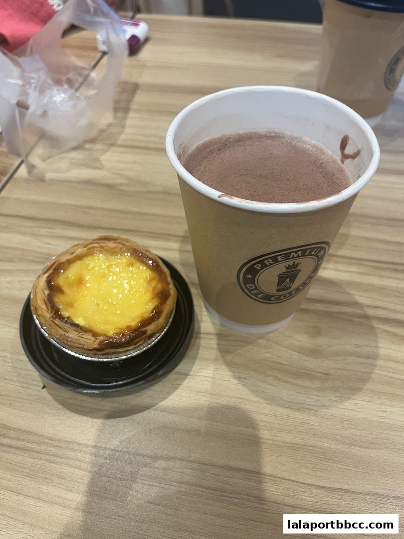 A close-up of a delicious egg tart and a cup of hot chocolate from Dee Coffee.