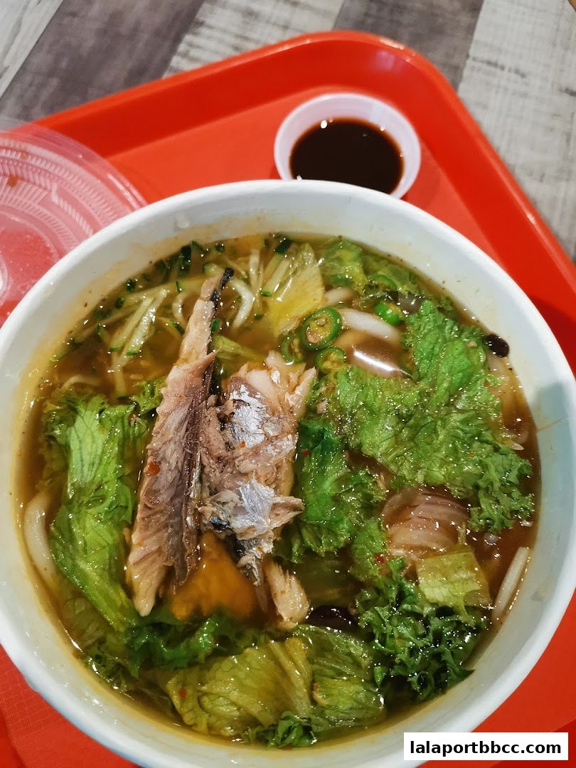 A bowl of delicious noodle soup with fish and fresh vegetables, served on a red tray.