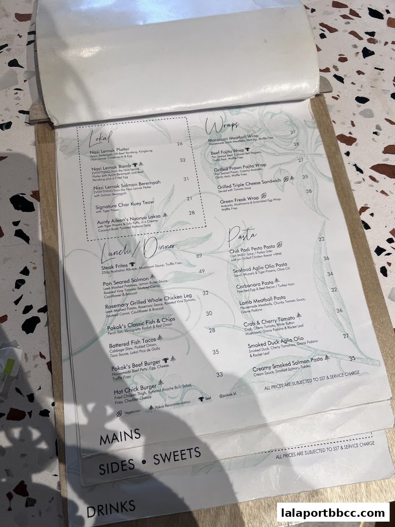 A menu from POKOK LaLaport featuring categories like Lokal, Wraps, Pasta, Mains, Sides, Sweets, and Drinks.