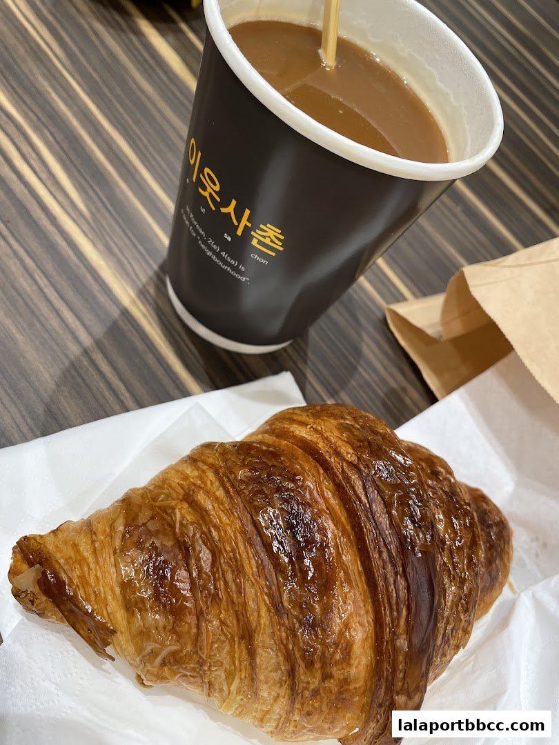 A golden-brown croissant and a cup of coffee with a wooden table background.