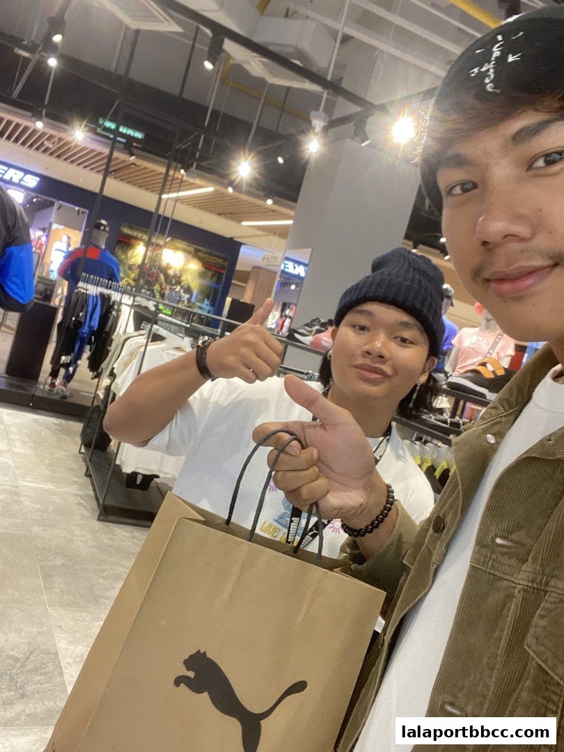Two young men are smiling and holding shopping bags inside a PUMA store.